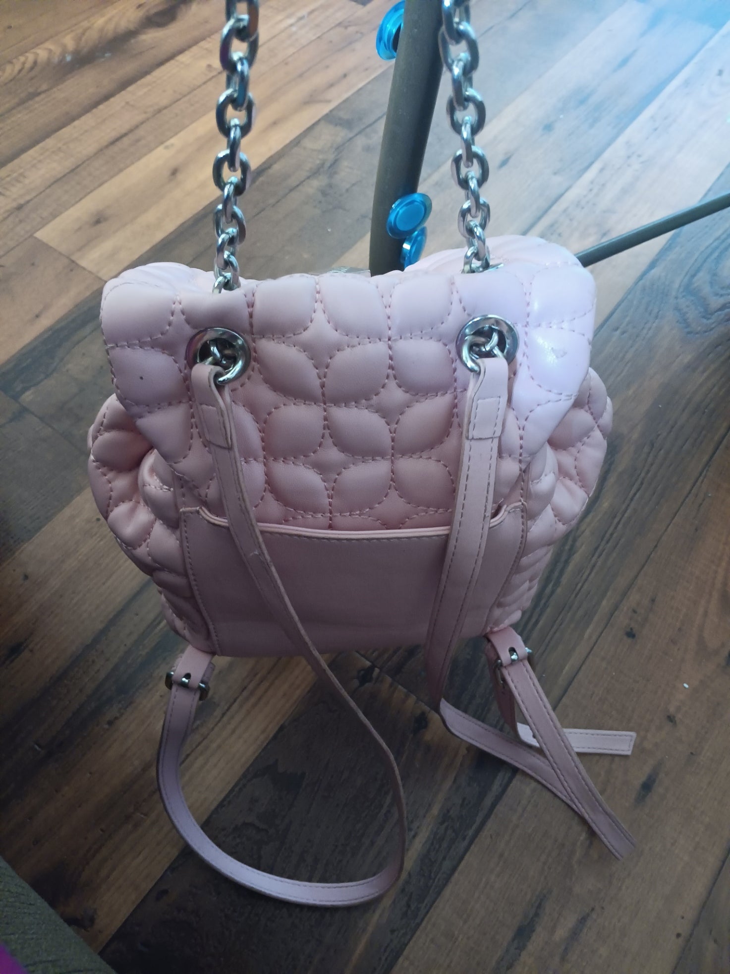 Pink quilted handbag with chain strap on a wooden surface